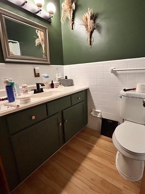 bathroom with toilet, wood finished floors, a wainscoted wall, tile walls, and vanity