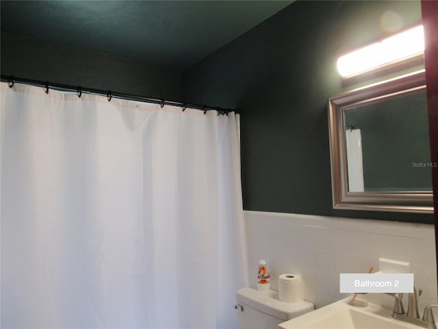full bath featuring toilet, tile walls, wainscoting, and a sink