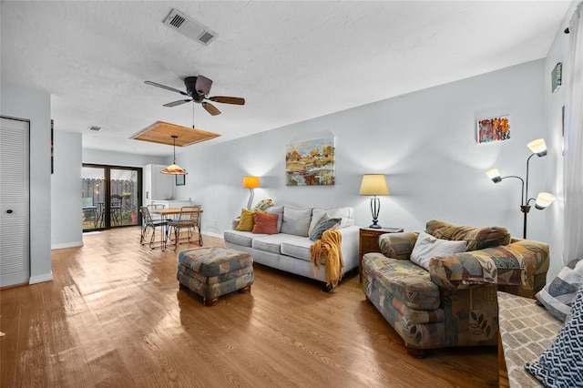 living room with wood finished floors, a ceiling fan, baseboards, and a textured ceiling