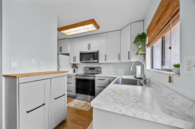 kitchen with appliances with stainless steel finishes, a sink, wood counters, dark wood-style flooring, and white cabinetry