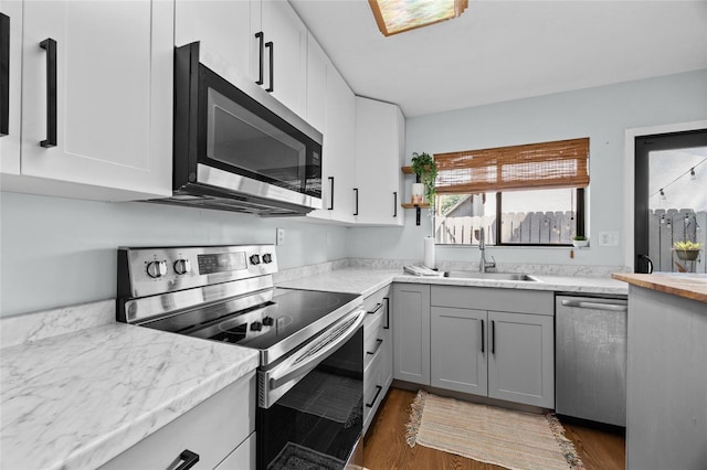 kitchen featuring stainless steel appliances, a sink, wood finished floors, gray cabinets, and white cabinetry