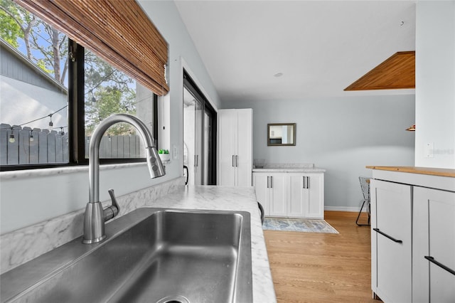 kitchen with a sink, white cabinetry, light countertops, light wood-type flooring, and baseboards