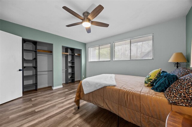 bedroom with wood finished floors, two closets, a ceiling fan, and baseboards