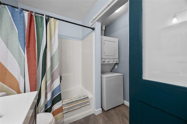 full bathroom featuring estacked washer and dryer, wood finished floors, toilet, shower / bath combo with shower curtain, and baseboards