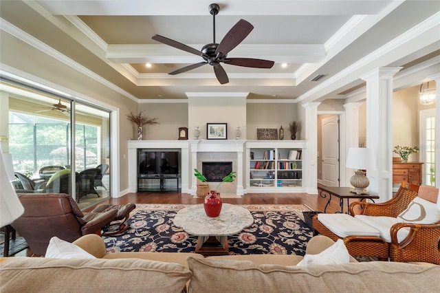 living room with wood finished floors, ceiling fan, ornate columns, crown molding, and a tiled fireplace