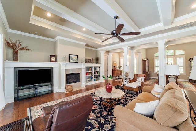 living area featuring ornate columns, ornamental molding, ceiling fan, wood finished floors, and a fireplace with flush hearth