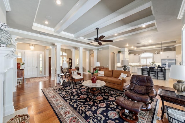 living room featuring crown molding, ceiling fan, light wood-style flooring, beamed ceiling, and ornate columns