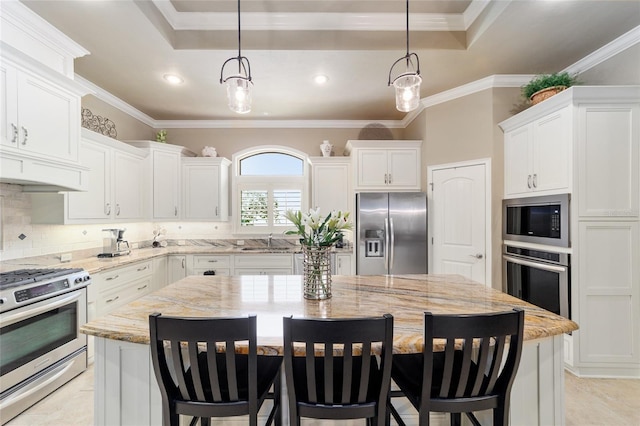 kitchen with appliances with stainless steel finishes, a sink, a kitchen island, white cabinets, and a breakfast bar