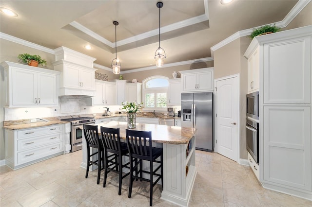 kitchen featuring stainless steel appliances, a tray ceiling, a kitchen island, white cabinetry, and crown molding