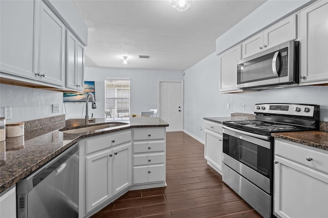 kitchen featuring dark wood finished floors, a sink, a peninsula, stainless steel appliances, and white cabinets