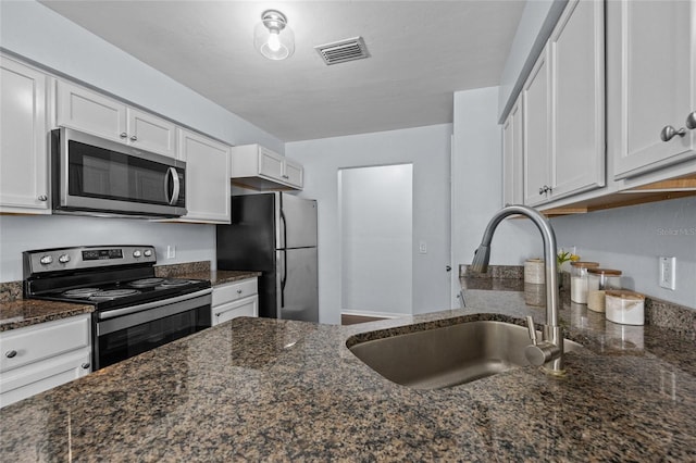 kitchen with visible vents, a sink, white cabinetry, dark stone counters, and appliances with stainless steel finishes