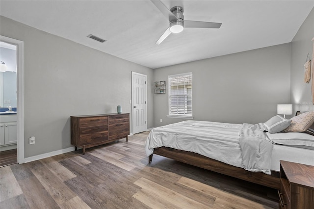 bedroom with baseboards, ensuite bathroom, visible vents, and wood finished floors