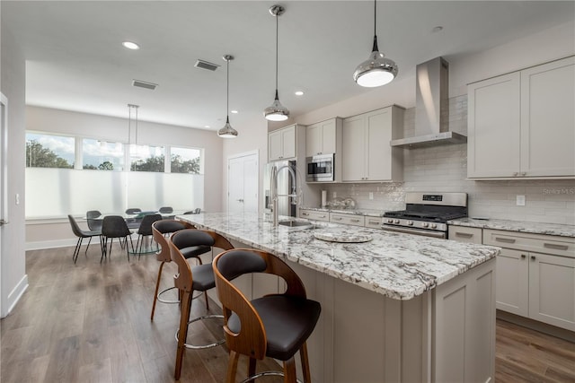 kitchen with a sink, appliances with stainless steel finishes, visible vents, and wall chimney exhaust hood