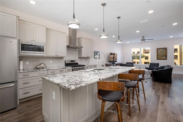 kitchen with a sink, stainless steel appliances, wall chimney range hood, decorative backsplash, and dark wood-style floors