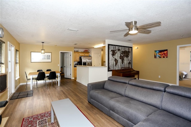 living area featuring a textured ceiling, ceiling fan, wood finished floors, and baseboards