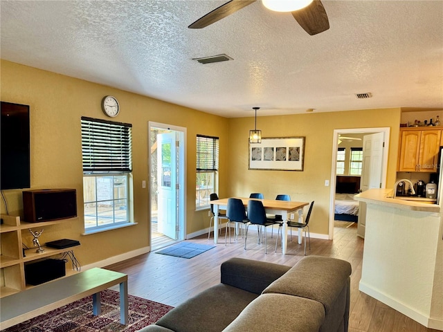 living room with healthy amount of natural light, light wood finished floors, a textured ceiling, baseboards, and ceiling fan