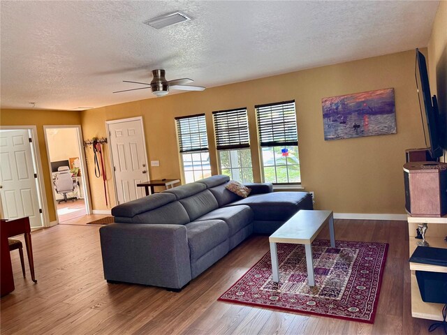 living room featuring a textured ceiling, wood finished floors, ceiling fan, and baseboards
