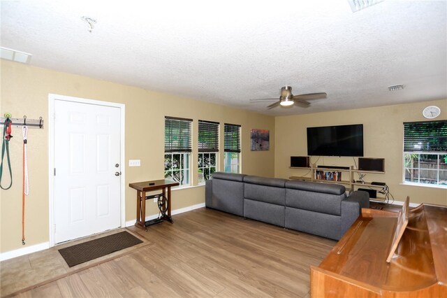 living room with plenty of natural light, ceiling fan, light wood-style floors, baseboards, and a textured ceiling