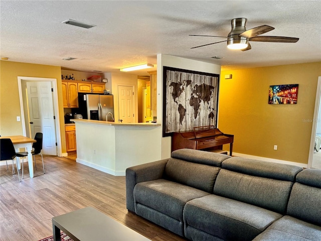 living room featuring a ceiling fan, a textured ceiling, light wood-style floors, and baseboards