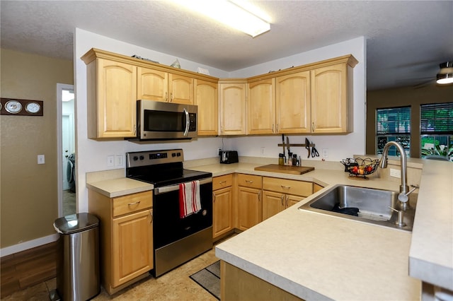 kitchen featuring stainless steel appliances, a sink, light brown cabinets, and a textured ceiling