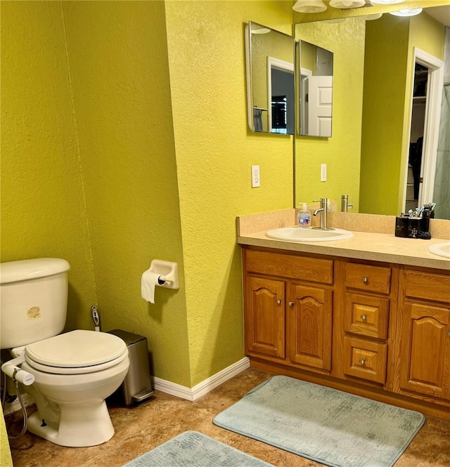 bathroom featuring a textured wall, toilet, double vanity, and baseboards