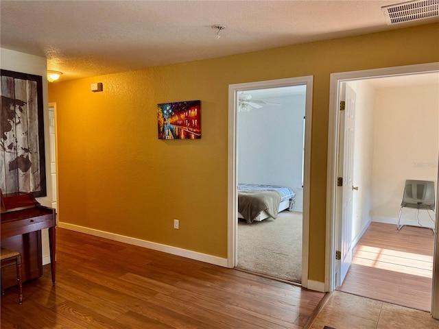 hall featuring wood finished floors, baseboards, and a textured ceiling