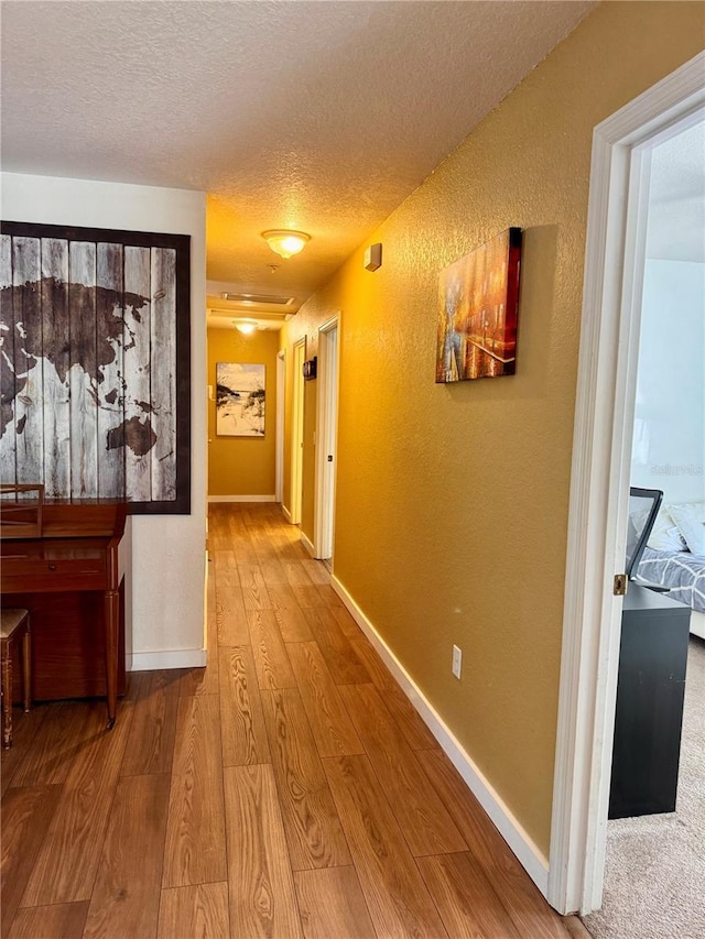 hall with a textured ceiling, wood-type flooring, a textured wall, and baseboards