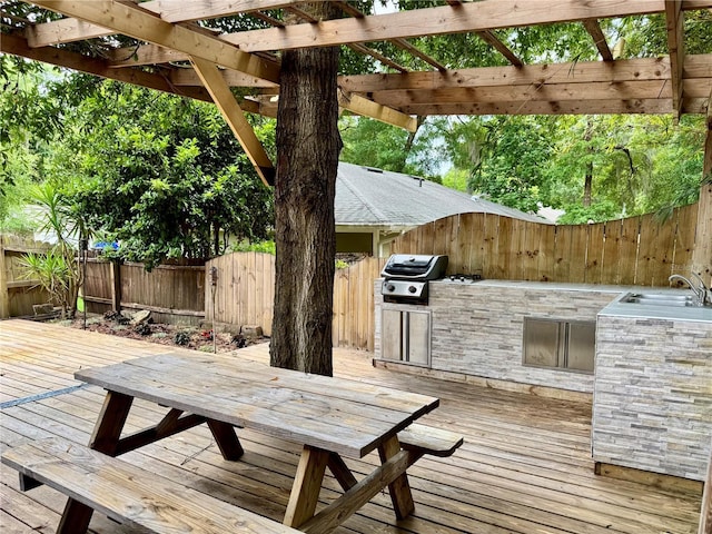 wooden deck featuring an outdoor kitchen, a fenced backyard, a grill, and a pergola