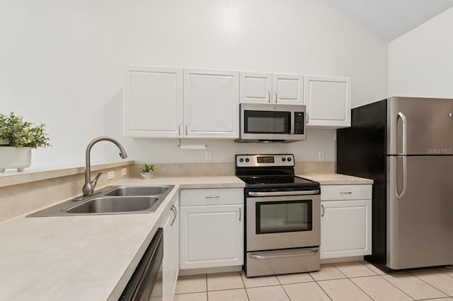 kitchen with appliances with stainless steel finishes, a sink, light tile patterned floors, white cabinets, and lofted ceiling