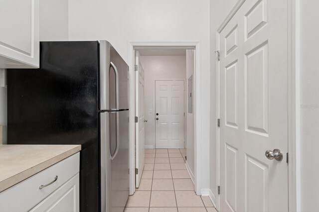 kitchen with freestanding refrigerator, light tile patterned flooring, white cabinetry, light countertops, and baseboards