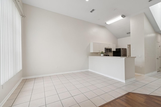 kitchen with stainless steel appliances, vaulted ceiling, white cabinetry, a peninsula, and light countertops