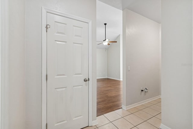 hall featuring baseboards, light tile patterned flooring, and lofted ceiling