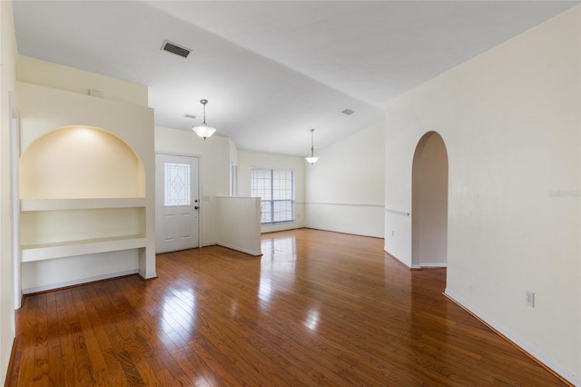 spare room featuring wood finished floors, visible vents, built in features, arched walkways, and lofted ceiling