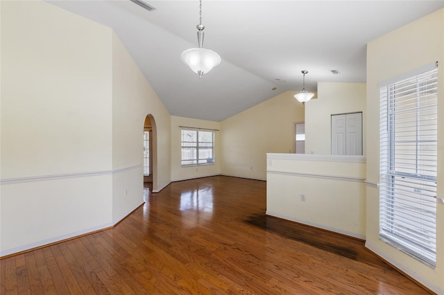 unfurnished room with wood finished floors, visible vents, baseboards, arched walkways, and vaulted ceiling