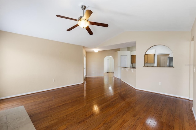 unfurnished living room featuring wood finished floors, vaulted ceiling, arched walkways, a ceiling fan, and baseboards