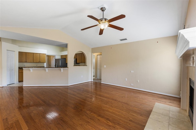 unfurnished living room featuring lofted ceiling, baseboards, a tiled fireplace, ceiling fan, and wood finished floors