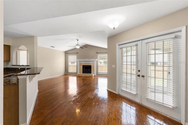unfurnished living room with vaulted ceiling, baseboards, a tiled fireplace, ceiling fan, and wood finished floors