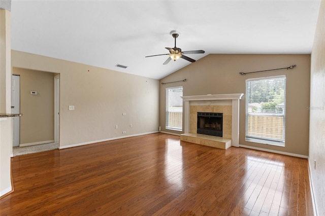 unfurnished living room featuring lofted ceiling, a tiled fireplace, ceiling fan, visible vents, and wood finished floors