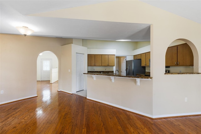 kitchen with a breakfast bar area, stainless steel fridge, brown cabinets, light wood-type flooring, and arched walkways
