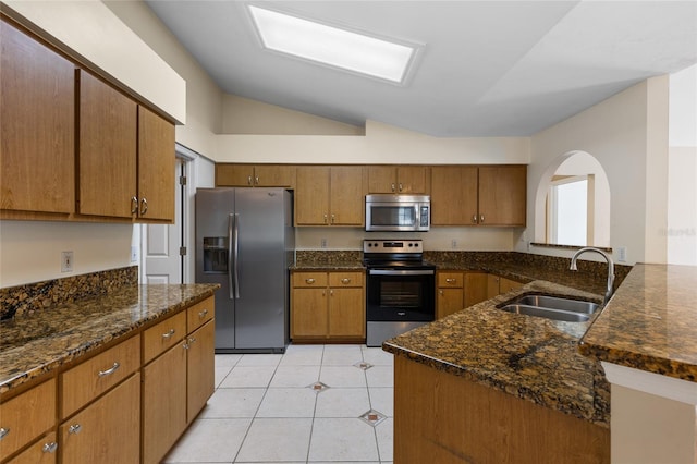 kitchen with brown cabinetry, a sink, vaulted ceiling, arched walkways, and stainless steel appliances