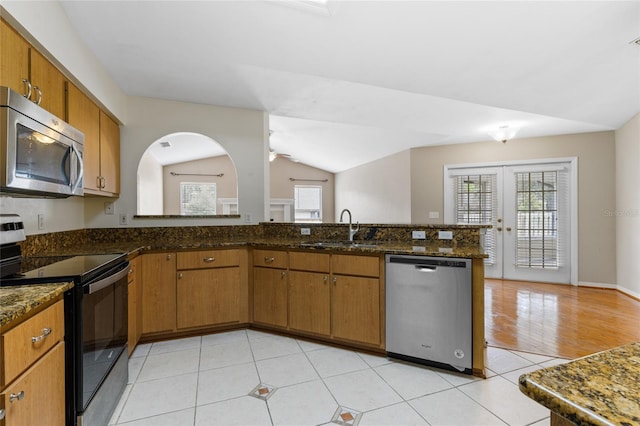 kitchen featuring a sink, a peninsula, brown cabinetry, dark stone countertops, and appliances with stainless steel finishes