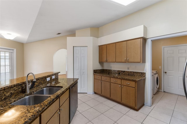 kitchen with independent washer and dryer, light tile patterned floors, a sink, dishwashing machine, and arched walkways
