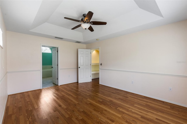 unfurnished bedroom featuring a raised ceiling, ensuite bathroom, visible vents, and wood finished floors