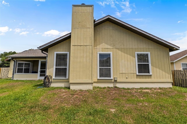 rear view of property with a yard, a chimney, and fence