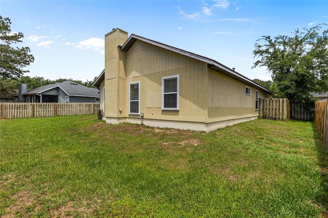 back of property featuring a fenced backyard, a yard, and a chimney