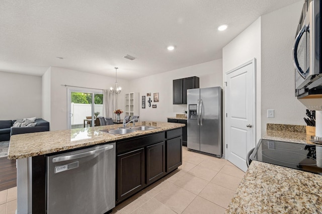 kitchen with a notable chandelier, light tile patterned floors, a sink, stainless steel appliances, and a kitchen island with sink