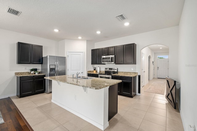 kitchen with a sink, stainless steel appliances, visible vents, arched walkways, and light stone counters