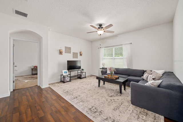 living area with a ceiling fan, a textured ceiling, visible vents, dark wood-type flooring, and arched walkways