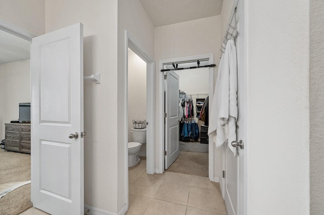 full bath with a walk in closet, toilet, baseboards, and tile patterned floors