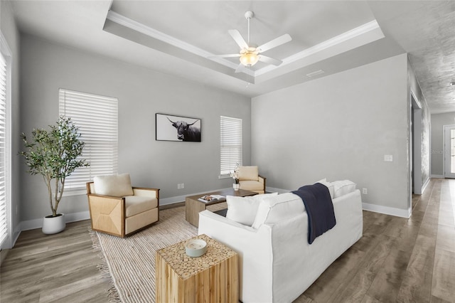 living area featuring a raised ceiling, wood finished floors, ceiling fan, baseboards, and ornamental molding